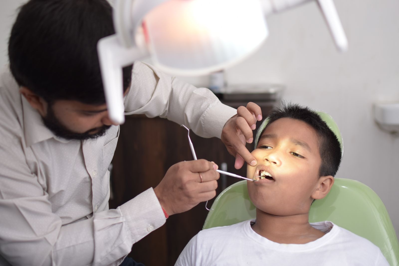 Um dentista examina os dentes de uma criança em uma clínica odontológica bem iluminada, focando nos cuidados orais.